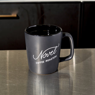 Black ceramic coffee mug with Novel Coffee Roasters logo.