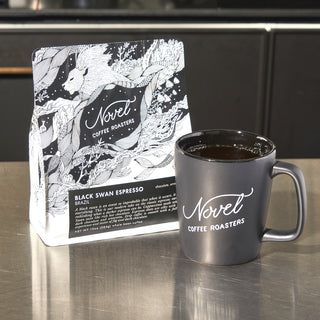 10 oz bag of black swan espresso next to a black branded ceramic mug.