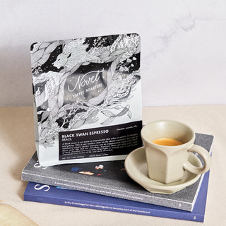Dark roasted Black Swan Espresso bag and demitasse stacked on top of coffee magazines.