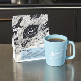 10 oz bag of tried and true filter blend next to a blue branded ceramic mug.