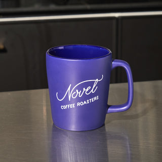 Purple ceramic coffee mug with Novel Coffee Roasters logo.