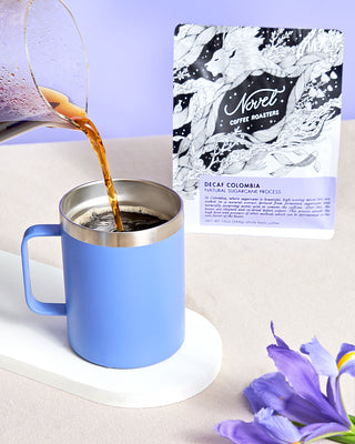 Carafe of natural sugarcane process decaf coffee being poured into a purple to-go mug.