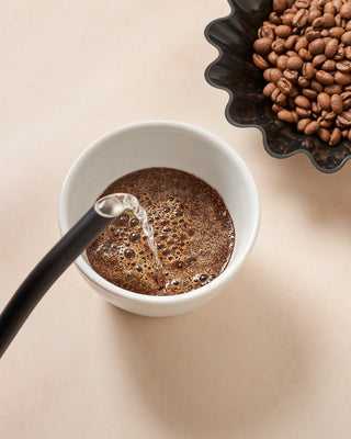 water pouring into a cupping vessel next to roasted coffee beans