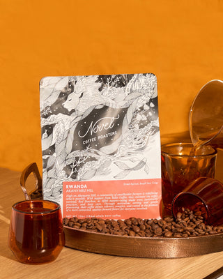 10 oz bag of coffee beans from Rwanda from Novel Coffee Roasters next to glasses of coffee and whole coffee beans